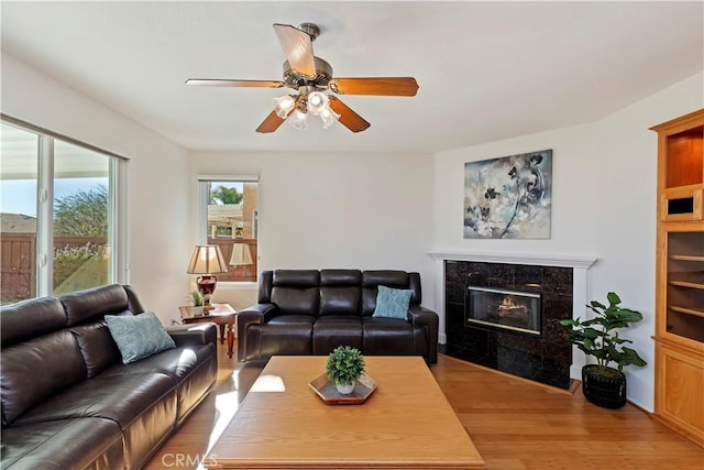 living room with a tiled fireplace, ceiling fan, and light hardwood / wood-style floors