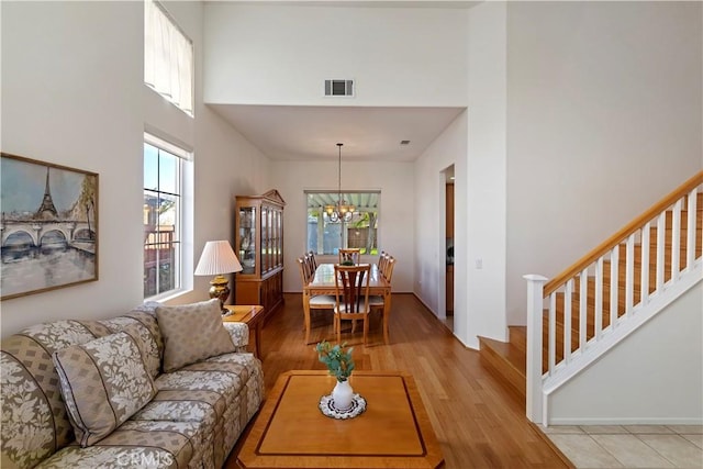 living room featuring a notable chandelier, light wood-type flooring, plenty of natural light, and a high ceiling