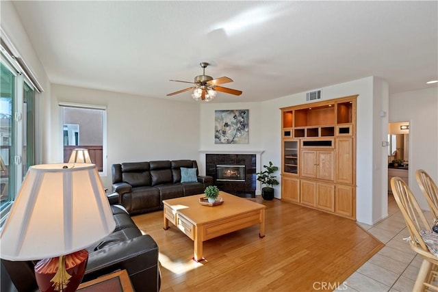 living room featuring light tile patterned floors, ceiling fan, built in shelves, and a fireplace