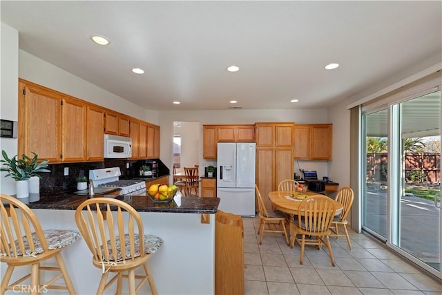 kitchen featuring white appliances, a kitchen breakfast bar, decorative backsplash, and light tile patterned floors