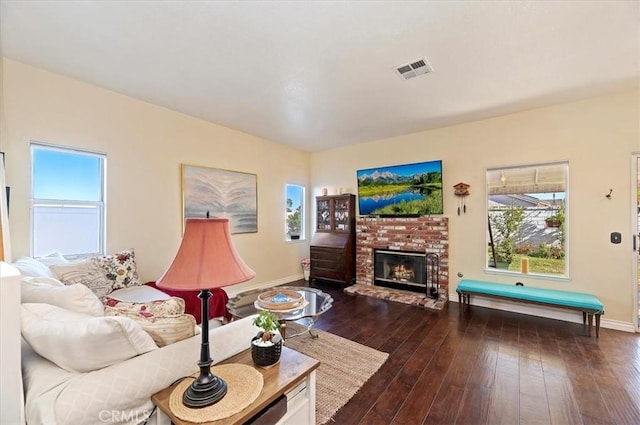 living room featuring a brick fireplace, dark hardwood / wood-style flooring, and plenty of natural light