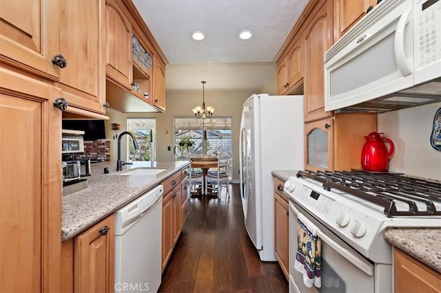 kitchen with white appliances, light stone counters, pendant lighting, a chandelier, and dark hardwood / wood-style floors