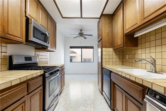 kitchen featuring sink, ceiling fan, stainless steel appliances, tile counters, and decorative backsplash