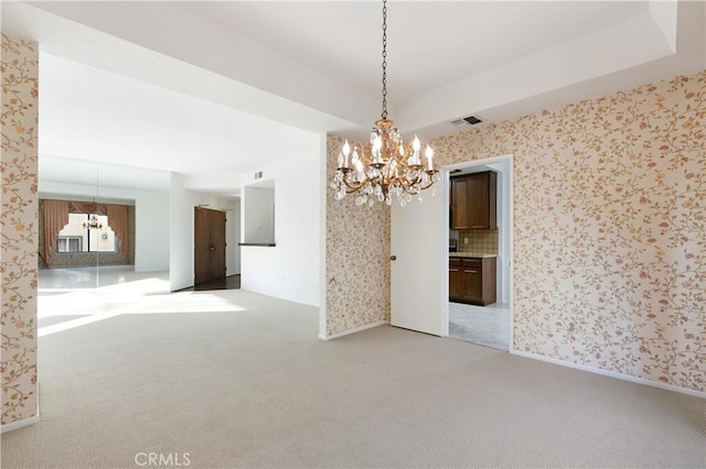 carpeted empty room with a raised ceiling and a chandelier