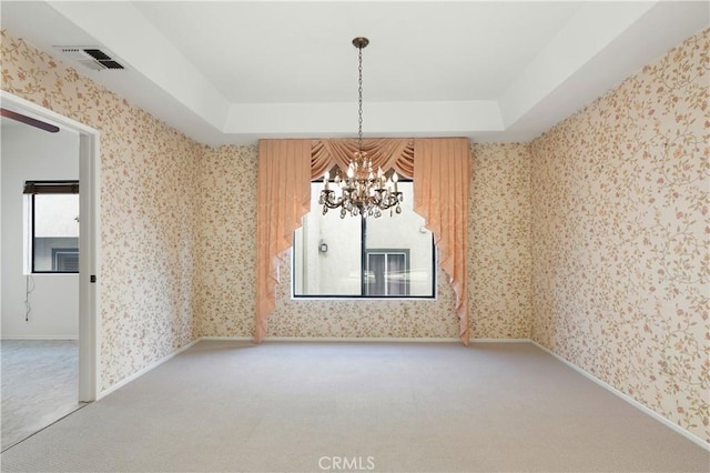 carpeted empty room with an inviting chandelier and a tray ceiling