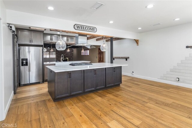 kitchen featuring sink, light hardwood / wood-style floors, a kitchen island, exhaust hood, and appliances with stainless steel finishes