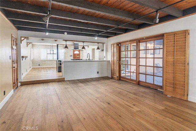 unfurnished living room featuring track lighting, beam ceiling, light hardwood / wood-style floors, and sink