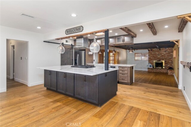 kitchen featuring a spacious island, stainless steel fridge with ice dispenser, a brick fireplace, beam ceiling, and dark brown cabinetry