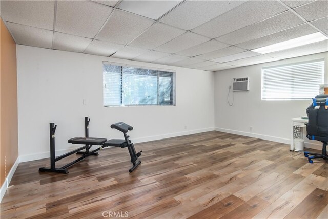 exercise room with a drop ceiling, hardwood / wood-style floors, a wealth of natural light, and a wall mounted air conditioner