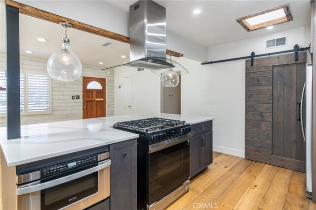 kitchen with stainless steel oven, black gas stove, island exhaust hood, hanging light fixtures, and a barn door