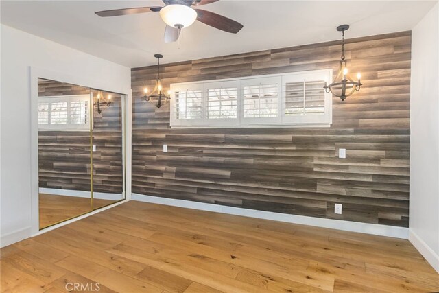 unfurnished room with ceiling fan with notable chandelier, wood-type flooring, and rustic walls