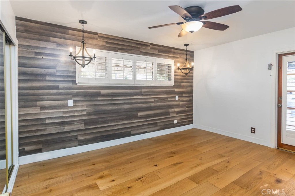 empty room featuring rustic walls, wood walls, ceiling fan with notable chandelier, and hardwood / wood-style flooring