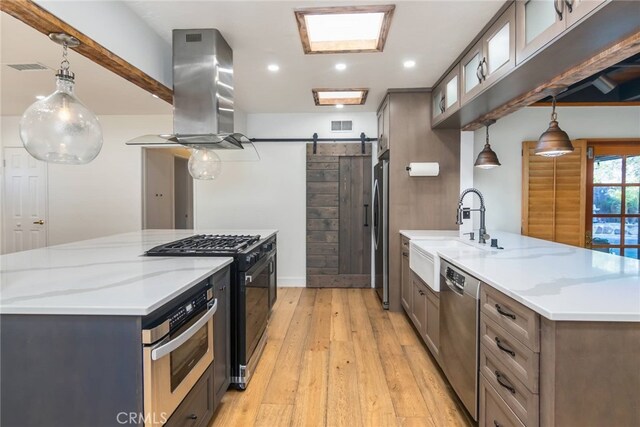 kitchen featuring stainless steel appliances, sink, light stone counters, island exhaust hood, and a barn door