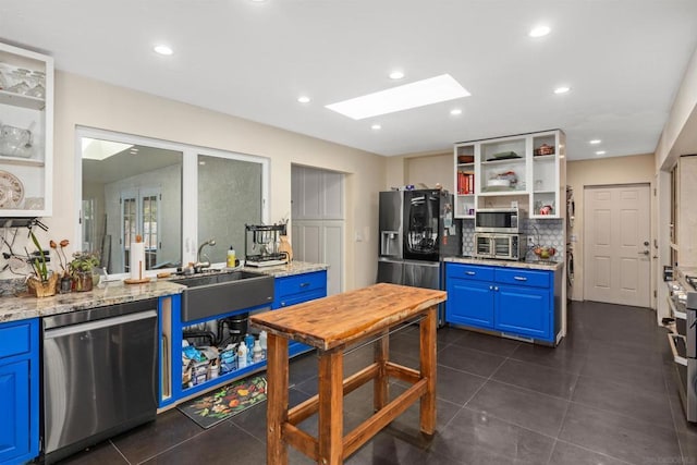 kitchen featuring appliances with stainless steel finishes, a skylight, light stone counters, and blue cabinetry