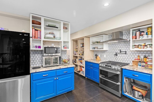 kitchen with stainless steel appliances, decorative backsplash, blue cabinetry, light stone countertops, and wall chimney range hood