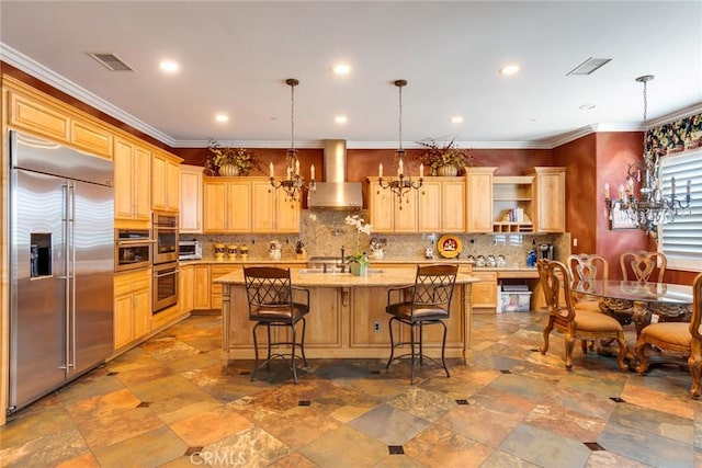 kitchen with wall chimney range hood, a breakfast bar, a notable chandelier, a center island with sink, and stainless steel built in fridge