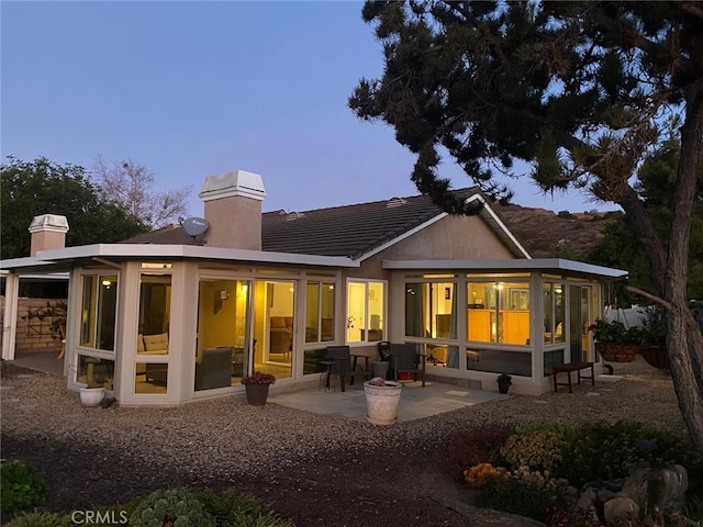 back house at dusk with a sunroom and a patio