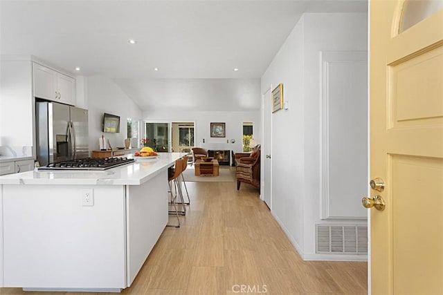 kitchen featuring vaulted ceiling, white cabinetry, light wood-type flooring, appliances with stainless steel finishes, and a kitchen breakfast bar