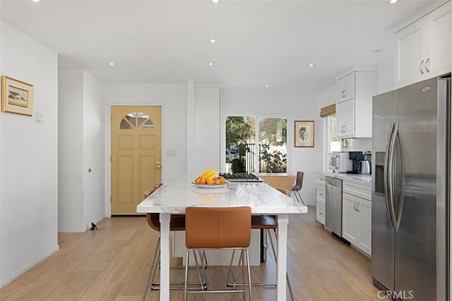 kitchen with a kitchen island, a breakfast bar, stainless steel appliances, white cabinets, and light stone counters