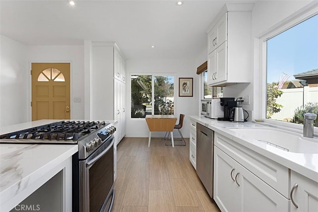 kitchen featuring appliances with stainless steel finishes, light wood-type flooring, light stone countertops, white cabinets, and sink