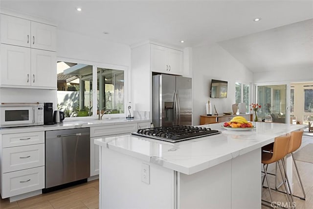 kitchen with white cabinets, appliances with stainless steel finishes, a center island, sink, and light stone counters