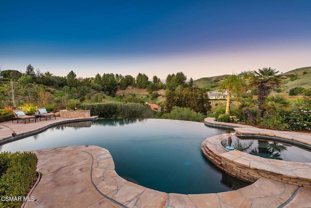 pool at dusk with a patio and an in ground hot tub