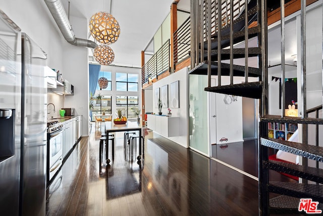 kitchen featuring a towering ceiling, white cabinetry, appliances with stainless steel finishes, wood-type flooring, and sink