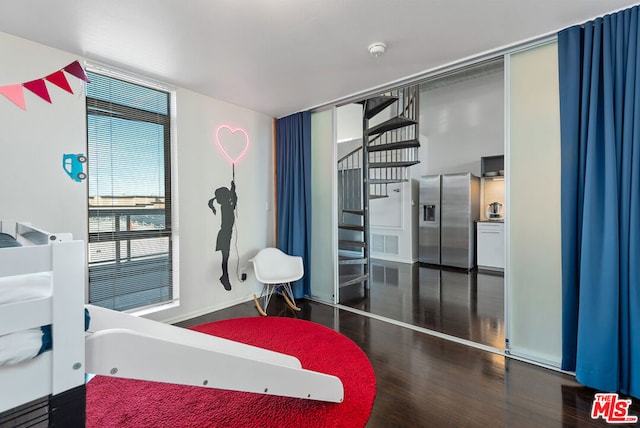 bedroom featuring dark hardwood / wood-style flooring, expansive windows, and stainless steel refrigerator with ice dispenser