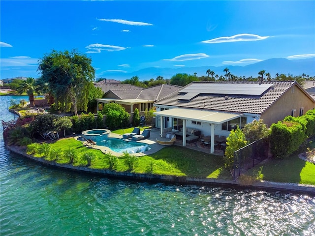 rear view of property featuring a lawn, solar panels, a water view, a swimming pool with hot tub, and a patio area