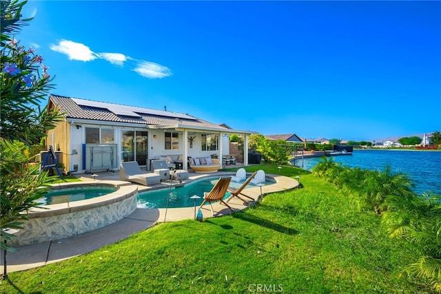 back of property with a swimming pool with hot tub, a water view, a lawn, solar panels, and a patio area