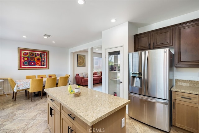 kitchen featuring a center island, light tile patterned floors, light stone counters, and stainless steel fridge