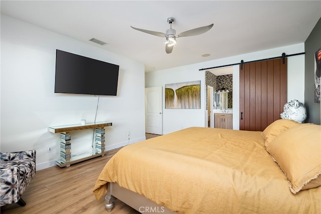 bedroom featuring ceiling fan, ensuite bathroom, a barn door, and wood-type flooring