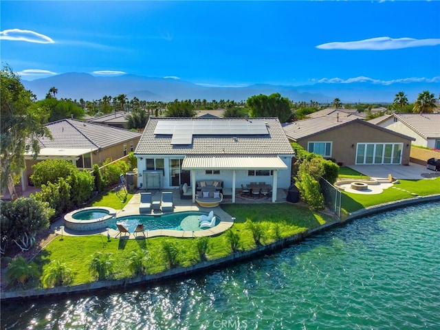 back of property with a pool with hot tub, solar panels, a patio area, and a water view