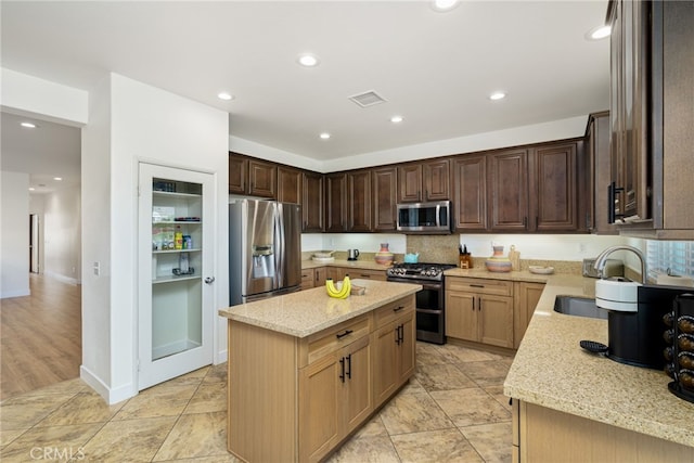 kitchen featuring stainless steel appliances, a center island, sink, and light stone countertops