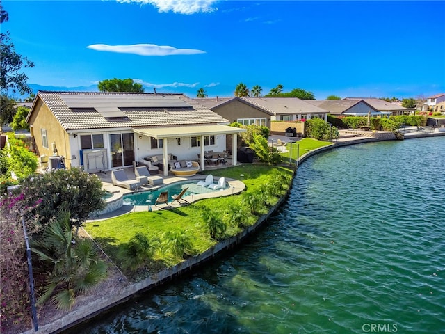 back of property featuring an outdoor hangout area, a patio, solar panels, a lawn, and a water view