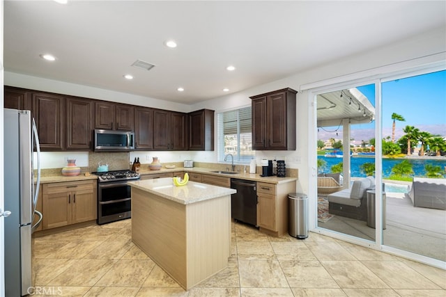 kitchen with light stone countertops, a kitchen island, appliances with stainless steel finishes, light tile patterned flooring, and sink