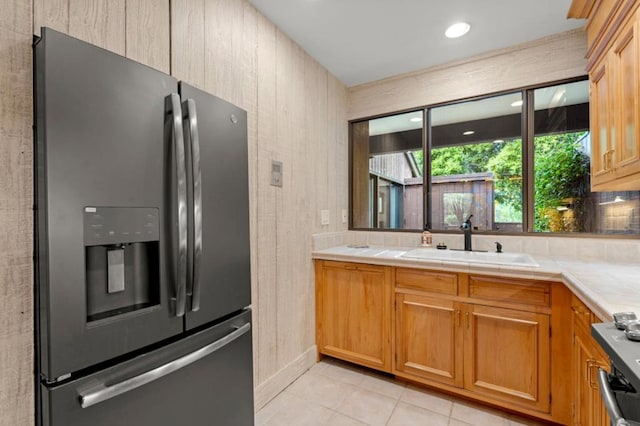 kitchen featuring stainless steel fridge with ice dispenser, light tile patterned floors, tile countertops, and sink