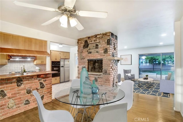 dining room with ceiling fan, a fireplace, and light hardwood / wood-style flooring