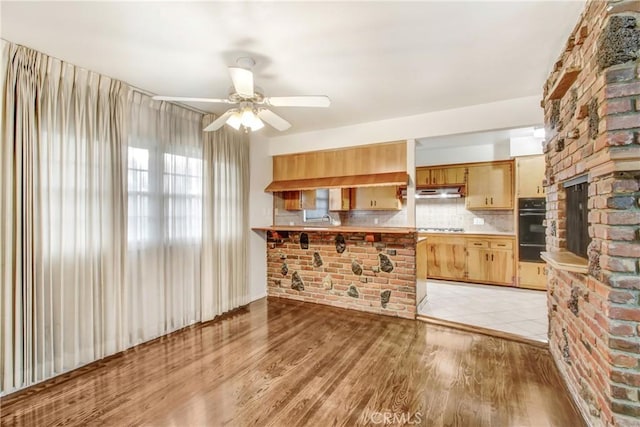 kitchen with kitchen peninsula, tasteful backsplash, sink, ceiling fan, and light hardwood / wood-style floors