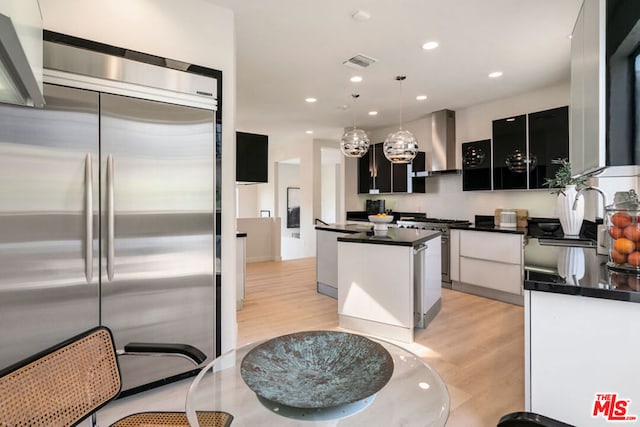 kitchen with stainless steel appliances, a center island, pendant lighting, light hardwood / wood-style flooring, and wall chimney range hood