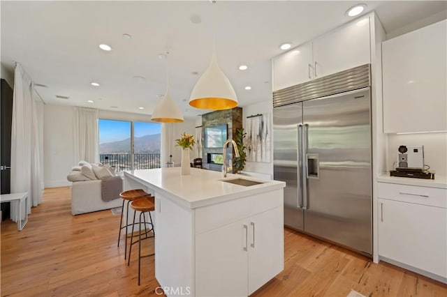 kitchen featuring white cabinets, a kitchen island with sink, built in fridge, and sink