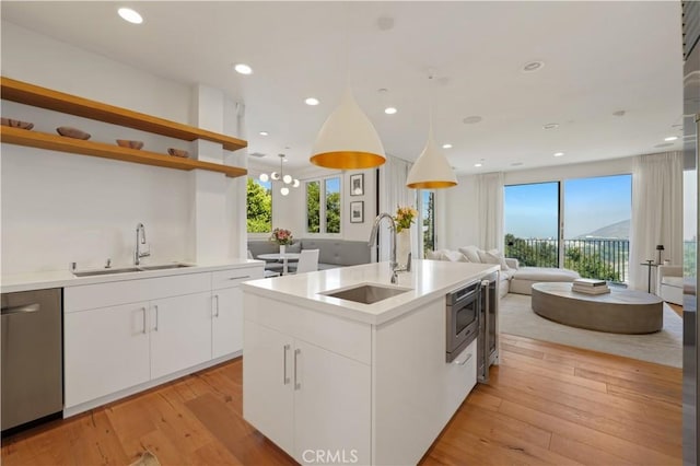 kitchen with hanging light fixtures, a kitchen island with sink, white cabinets, appliances with stainless steel finishes, and sink