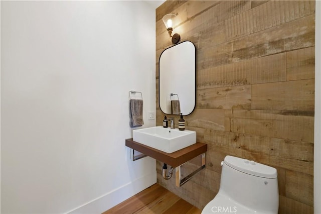 bathroom featuring toilet, wood-type flooring, wooden walls, and sink