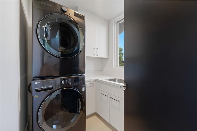 clothes washing area with cabinets, light tile patterned flooring, and stacked washer and clothes dryer