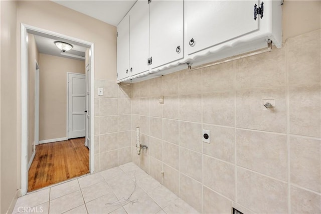 clothes washing area featuring light tile patterned floors and cabinets