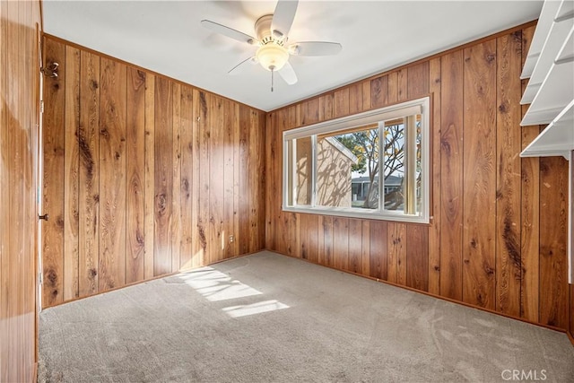 carpeted empty room featuring ceiling fan and wooden walls