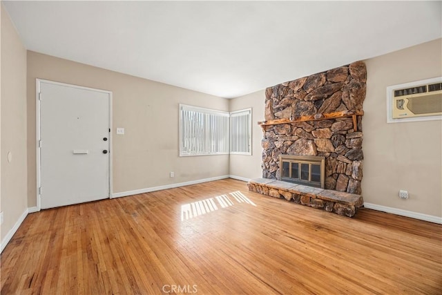 unfurnished living room featuring a wall unit AC, light hardwood / wood-style floors, and a stone fireplace