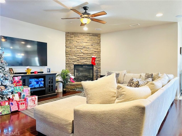 living room featuring ceiling fan, a stone fireplace, and dark hardwood / wood-style floors