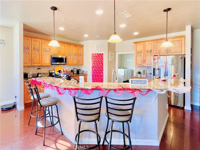 kitchen with a center island with sink, appliances with stainless steel finishes, washer and dryer, and hanging light fixtures