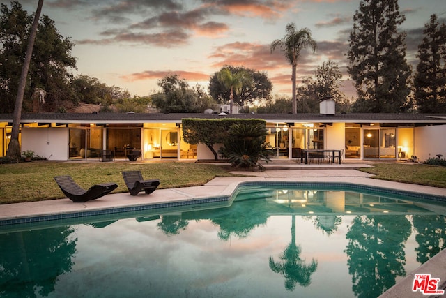 pool at dusk featuring a lawn and a patio area